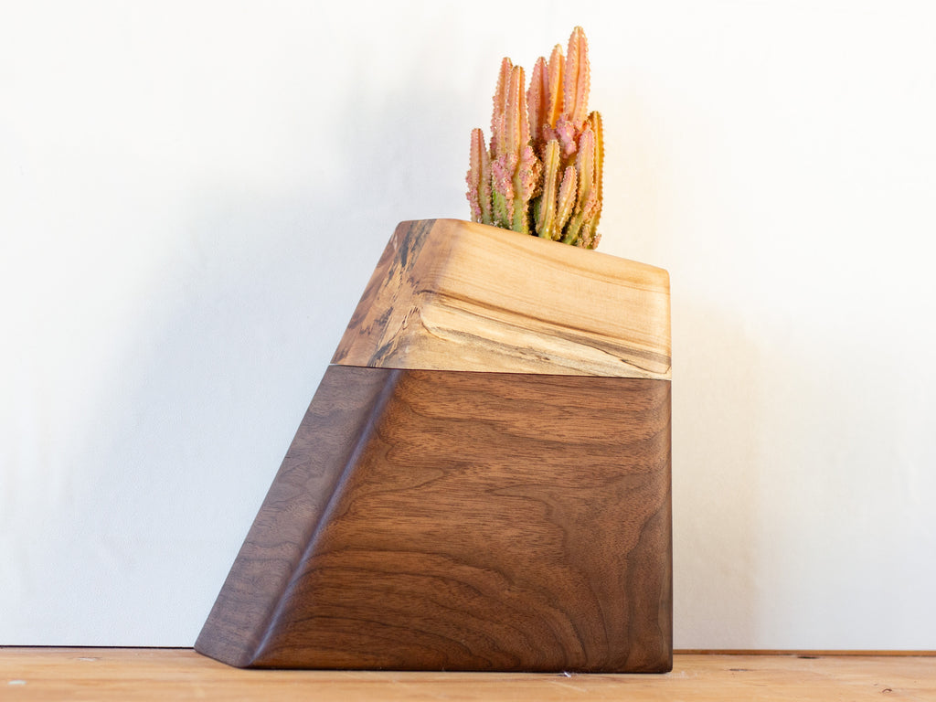 Modern cremation urn handcrafted from rich, FSC-certified Walnut with a minimalist, sculptural design. Features a hidden compartment for ashes and a recessed space on top for a living plant, blending natural materials with contemporary aesthetics.